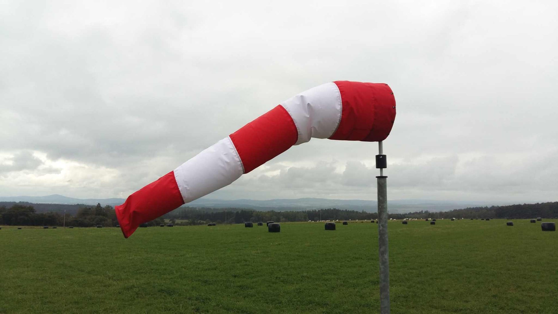 Windsackhülle in Rot-Weiß auf Feld montiert, zeigt Windrichtung; UV-stabilisiert, wasserabweisend.