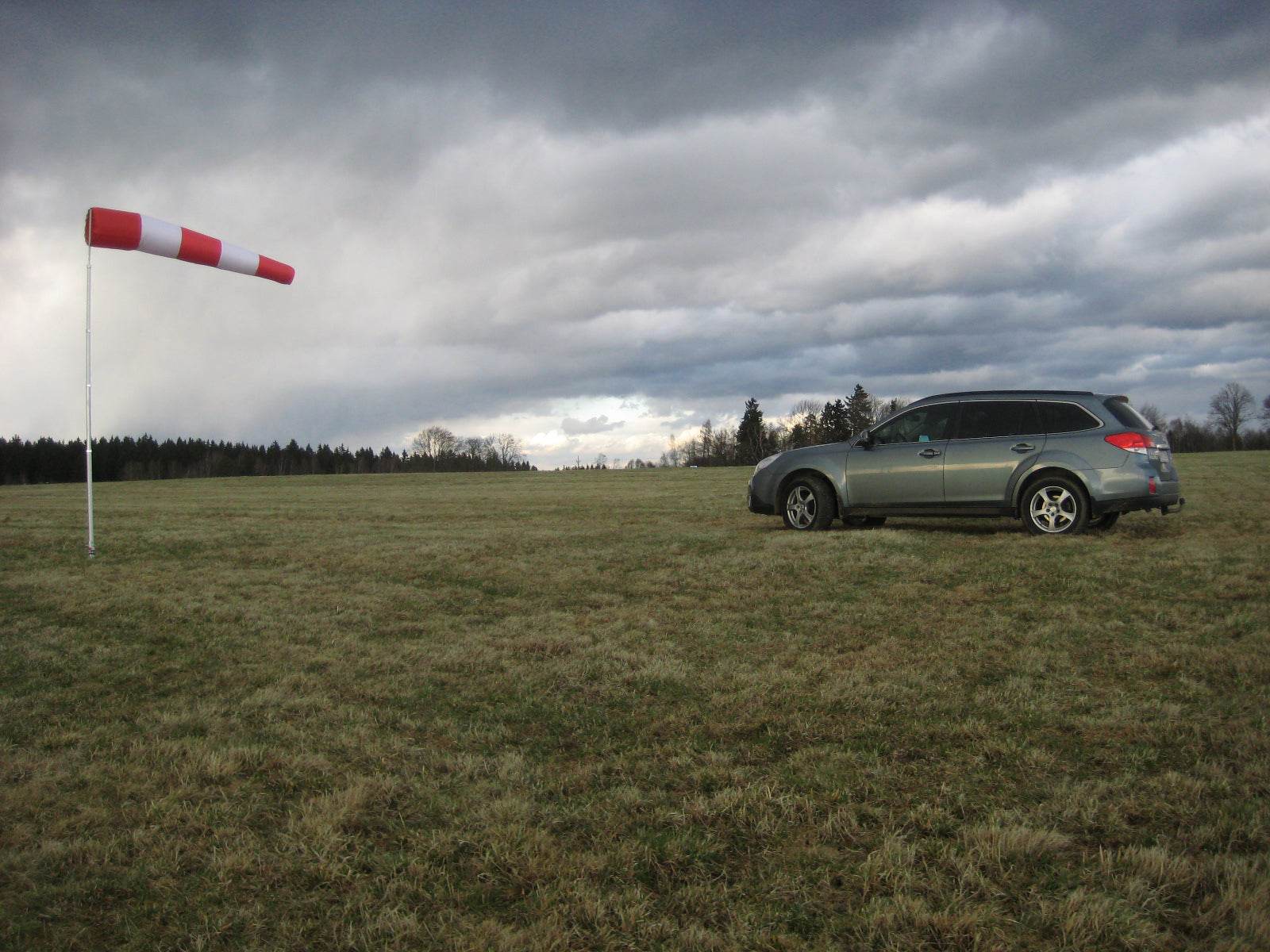 Windsackhülle auf offener Wiese neben einem Auto unter wolkigem Himmel.